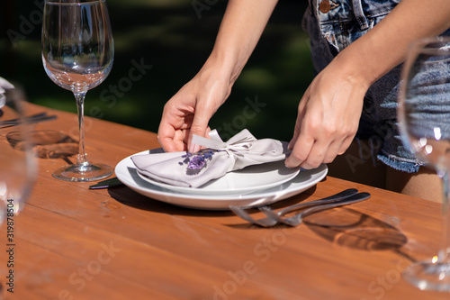 Girl the waiter in a summer cafe under the open sky sets the dishes on a wooden table.