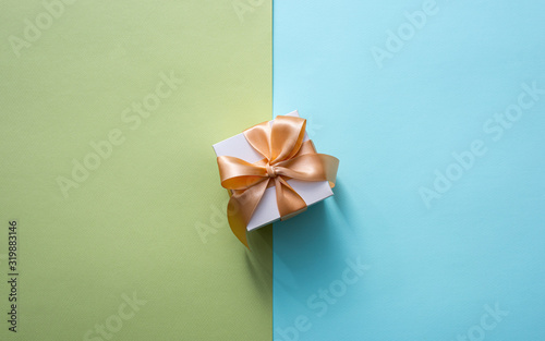Gift box with golden tied bow, on two-color background. Top view holiday background.