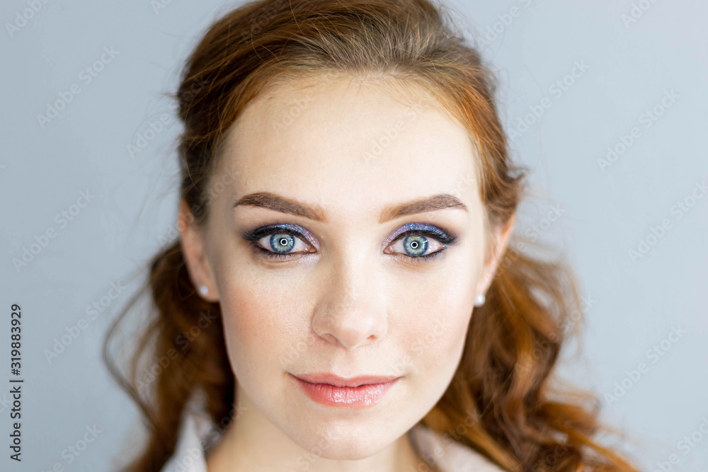Ginger model with bright make-up and wavy hairstyle. Fashion highlighter on skin, sexy gloss lips, dark eyebrows. Posing on gray background, close up Ginger model with bright make-up and wavy hairstyle. Fashion highlighter on skin, sexy gloss lips, dark eyebrows. Posing on gray background, close up