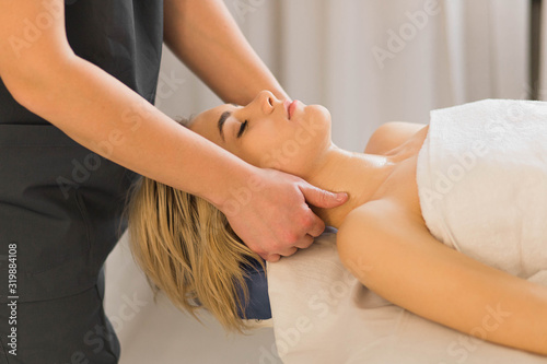 Hands of masseur making therapeutic neck massage for woman lying on couch in beauty spa salon. Body correction  treatments and relaxing. Close up