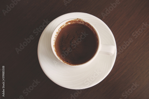 little white cup with hot black coffee on a brown table