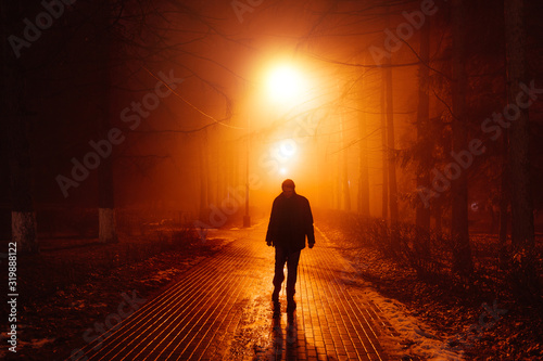 Sad man alone walking along the alley in night foggy park. Front view © Mulderphoto