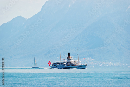 Excursion water ferry with Swiss flag on Lake Geneva at Ouchy embankment in Lausanne, Switzerland. People aboard