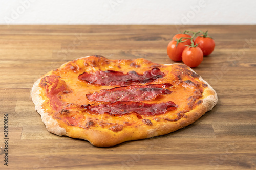 perfectly baked homemade pizza with tomato sauce, mozzarella, beef ham and arugula on a wooden table decorated with fresh tomatoes