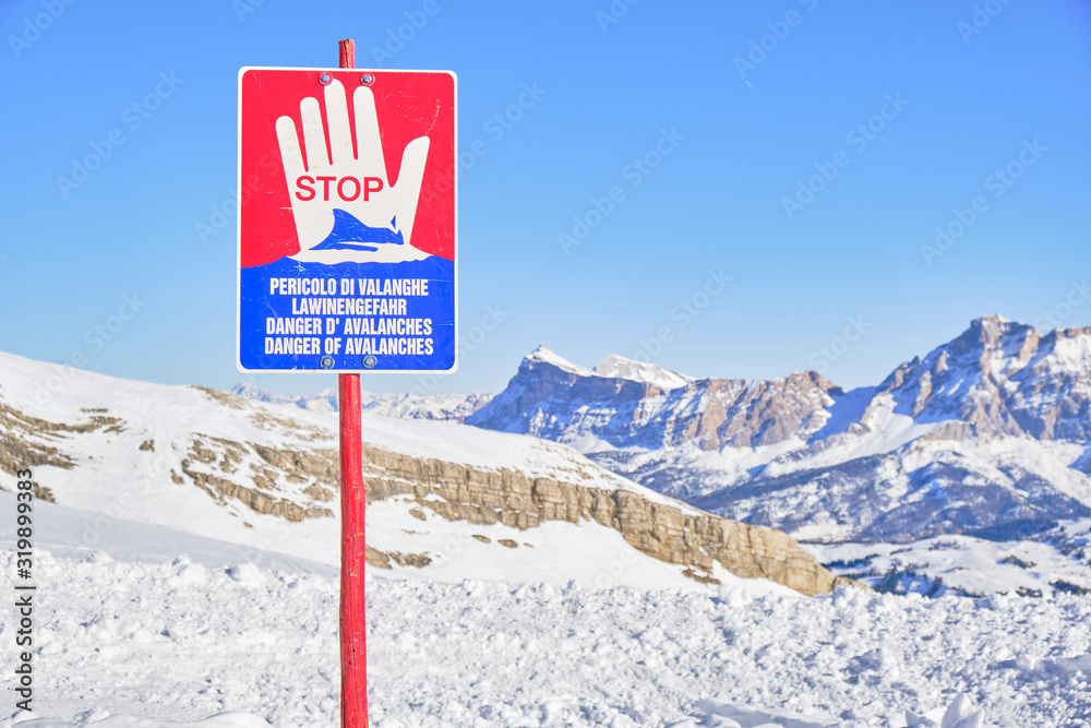 Avalanche warning stop sign saying Danger of Avalanches in Italian, German, French, and English languages, high up in the Dolomites mountains, Italy.