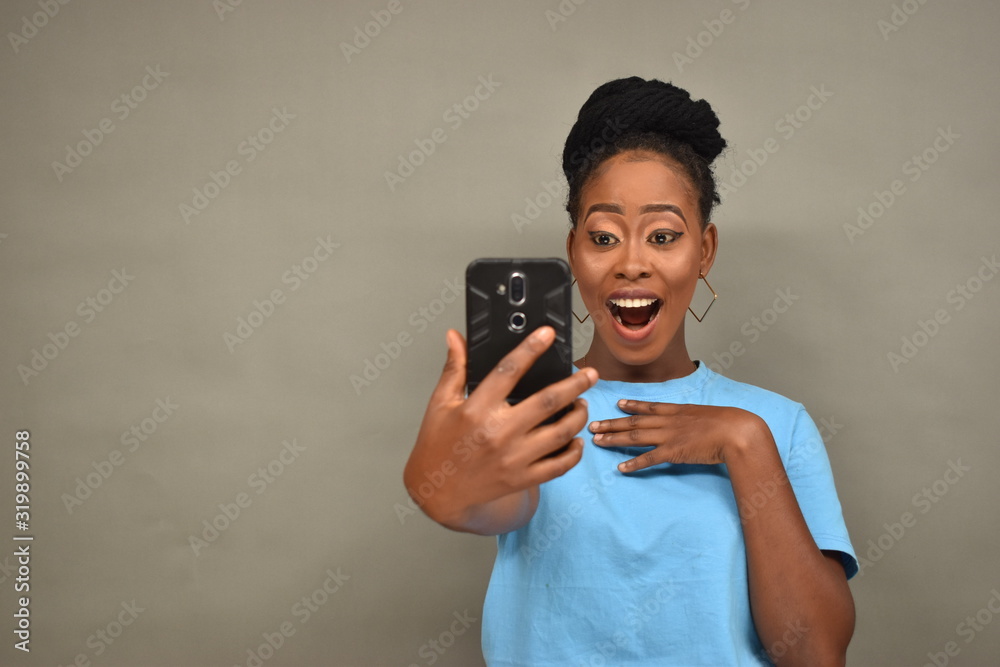 pretty african woman viewing content on her mobile phone feeling happy and excited, looking surprised