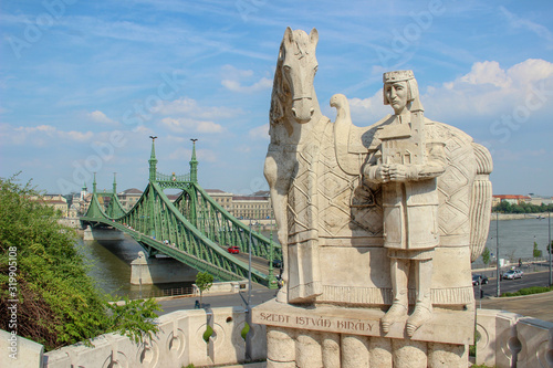 Statue of King Saint Stephen (St Steven, Szent István Király) on Gellért hill and the green Liberty bridge (Szabadság híd) over Danube river. View from the Citadella. Budapest, Hungary.