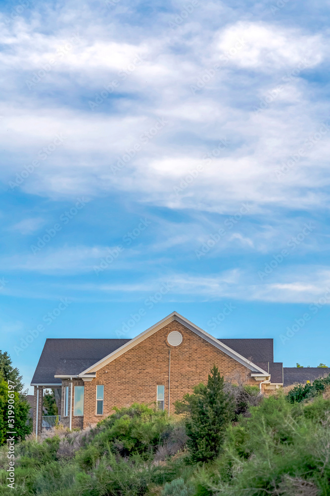 Blue sky and clouds over a home with gray roof and brick exterior wall Blue sky and clouds over a home with gray roof and brick exterior wall