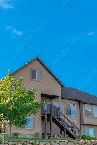 Home exterior with gable and valley roof against vibrant blue sky on a sunny day © Jason