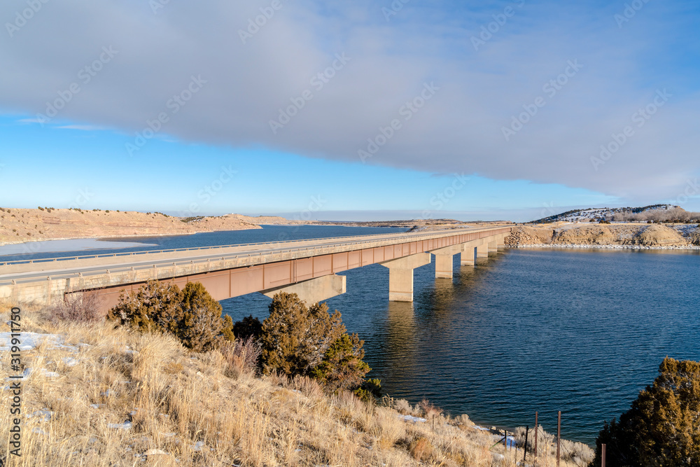 Bridge over lake connecting hills covered with snow on a sunny winter day Bridge over lake connecting hills covered with snow on a sunny winter day