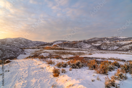 Hill landscape blanketed with snow and illuminated by sunlight at sunset