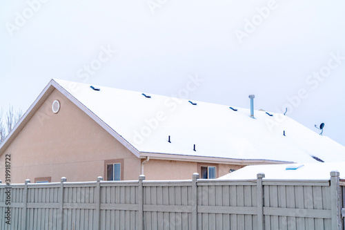 Home exterior with gable roof blanketed with snow against cloudy sky in winter