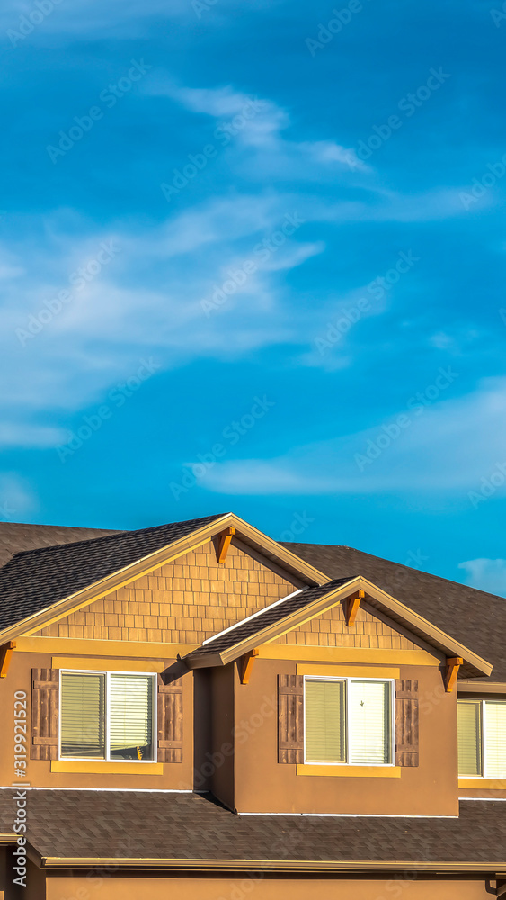 Vertical House exterior with dormers and gray roof against hills and cloudy blue sky Vertical House exterior with dormers and gray roof against hills and cloudy blue sky