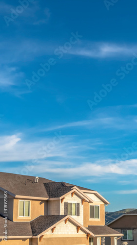 Vertical Vibrant blue sky with clouds over houses and hill viewed on a sunny day © Jason