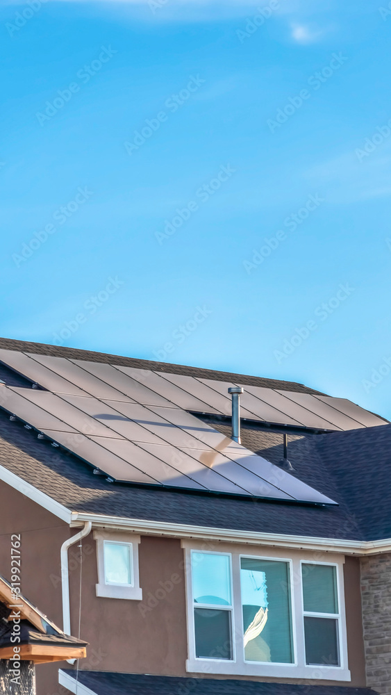 Vertical frame Gray roof of home with solar panels and pipe vents against blue sky background Vertical frame Gray roof of home with solar panels and pipe vents against blue sky background
