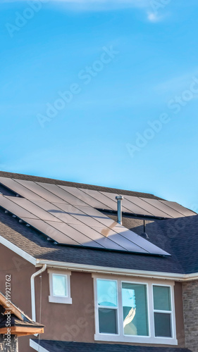 Vertical frame Gray roof of home with solar panels and pipe vents against blue sky background