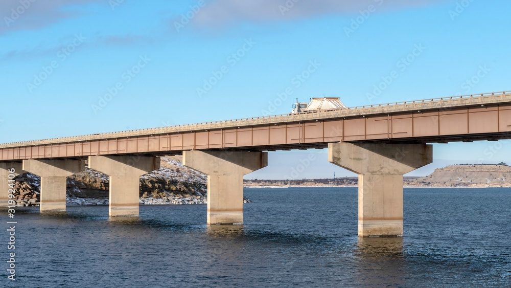 Panorama Truck travelling on a beam bridge over lake against rugged land and cloudy sky