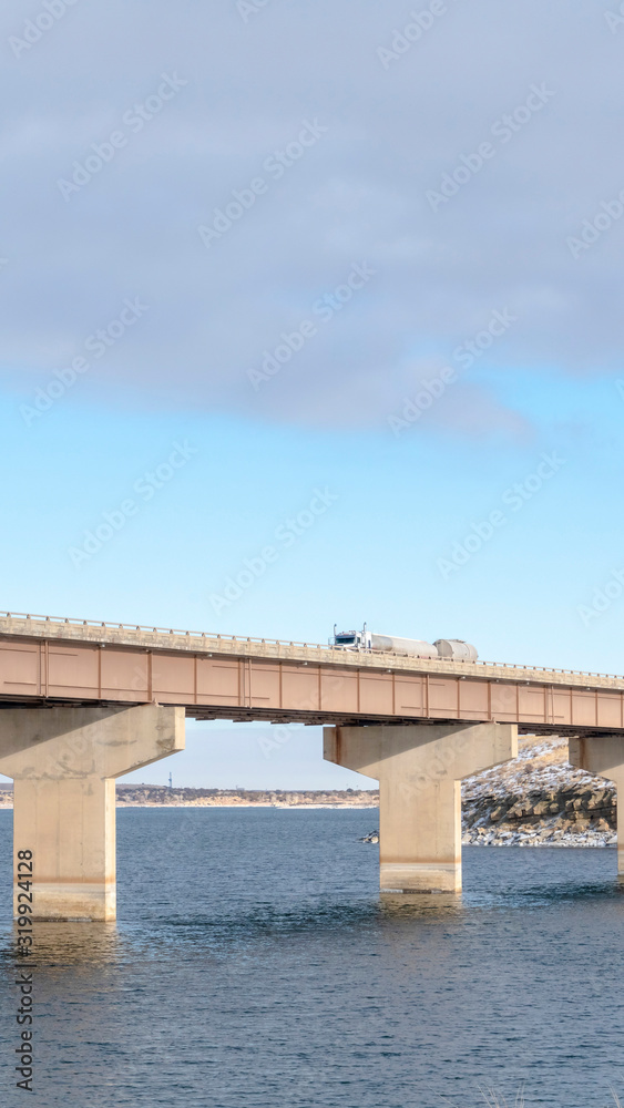 Vertical frame Stringer bridge supported by abutments ovelooking lake land and cloudy sky Vertical frame Stringer bridge supported by abutments ovelooking lake land and cloudy sky
