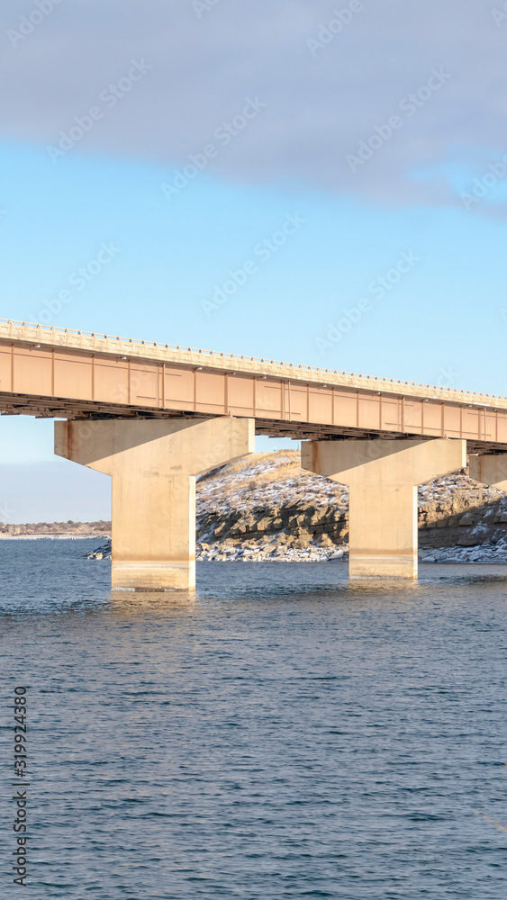 Vertical frame Stringer bridge crossing over a blue lake and connecting snowy rocky terrains Vertical frame Stringer bridge crossing over a blue lake and connecting snowy rocky terrains