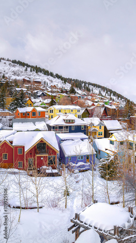 Vertical Colorful homes and scenic hills blanketed with white snow during winter season © Jason
