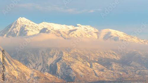 Panorama Amazing winter view of Mount Timpanogos against sky with snowy peak above clouds © Jason