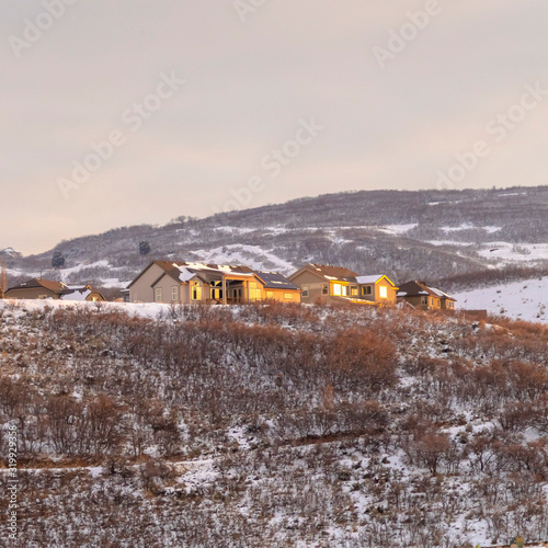 Fototapeta Naklejka Na Ścianę i Meble -  Photo Square frame Homes on grassy and snowy hills against cloudy sky on a frosty winter day