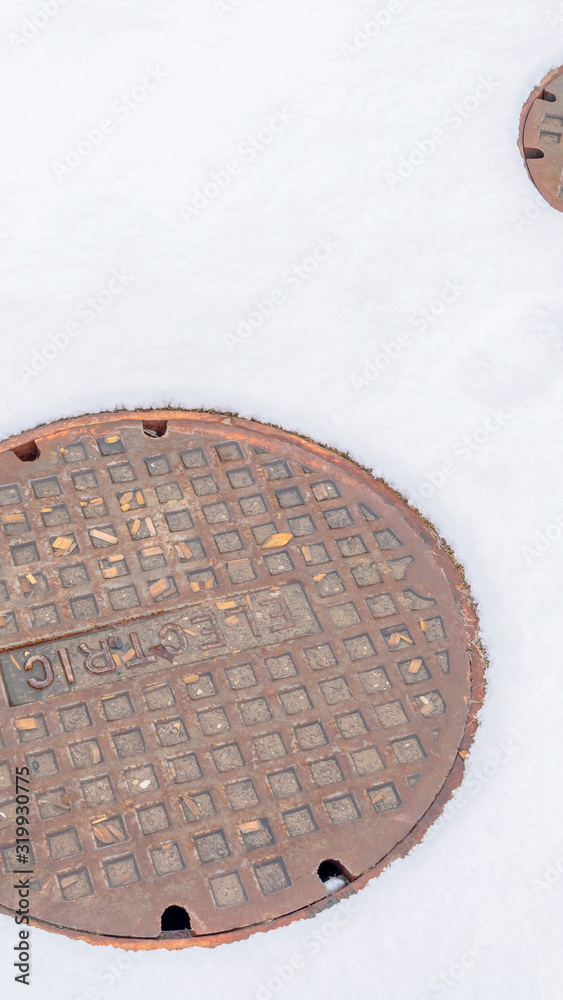 Photo Vertical Electric manhole covers surrounded by a sheet of snow during winter season