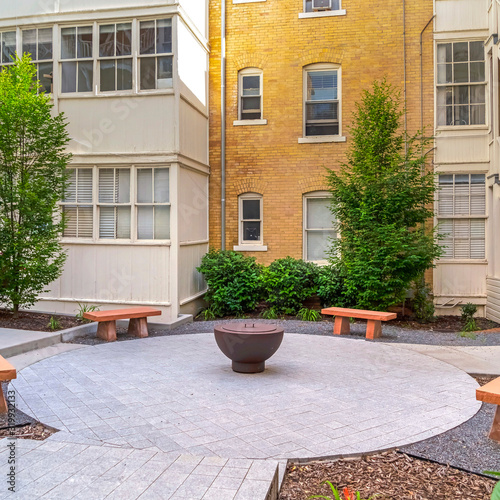 Square Stone benches around a fire pit outside a residential building on a sunny day © Jason