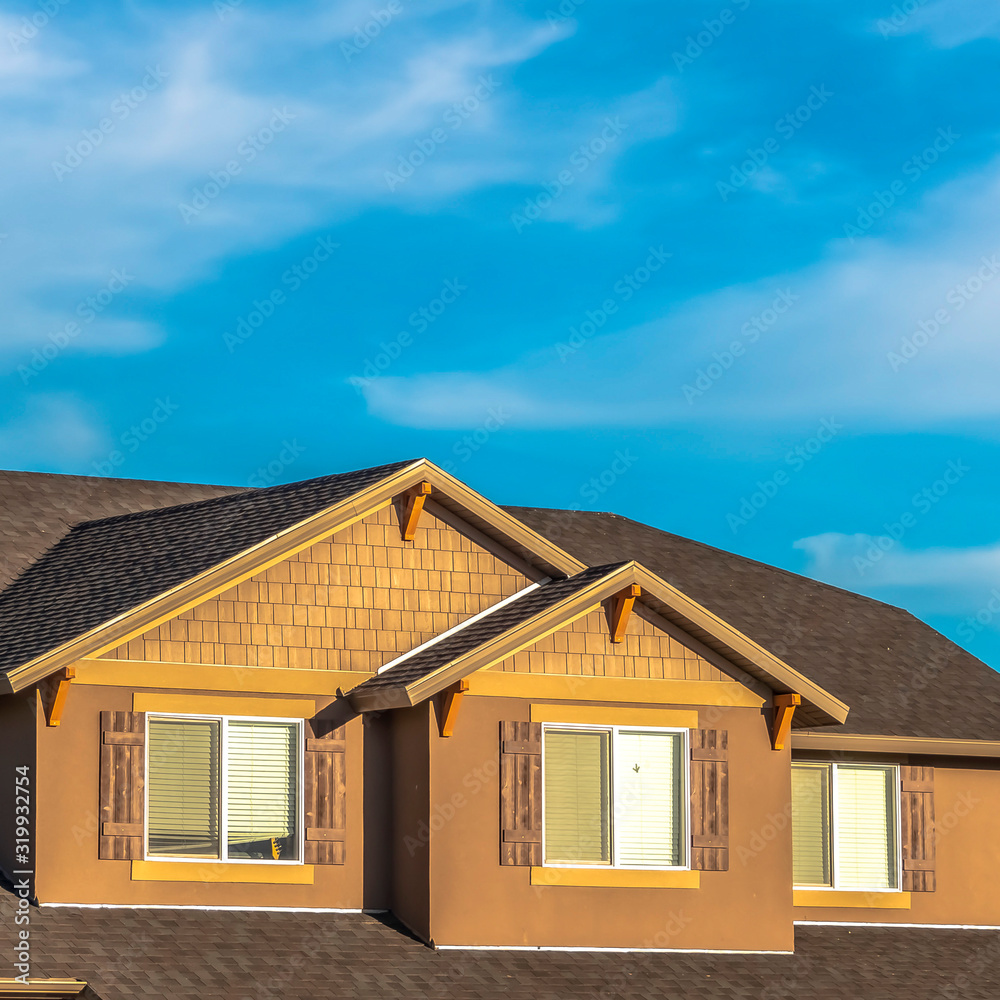 Square frame House exterior with dormers and gray roof against hills and cloudy blue sky Square frame House exterior with dormers and gray roof against hills and cloudy blue sky