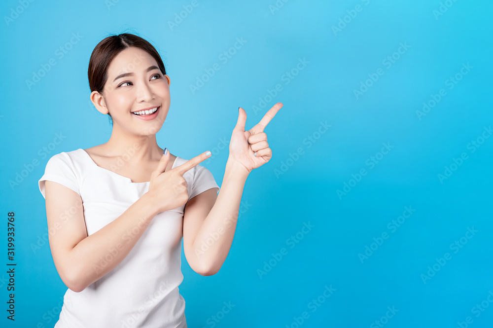 Beautiful young asian stand and pointing to copy space with big smile happy beaming face in seamless blue isolated background. Beautiful young asian stand and pointing to copy space with big smile happy beaming face in seamless blue isolated background.