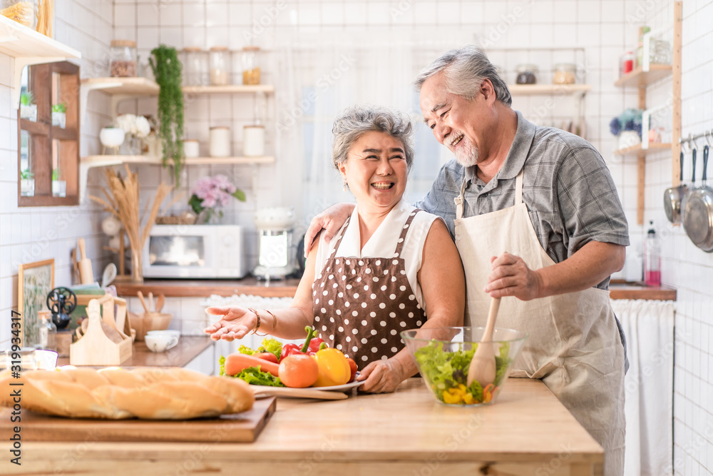 Couple senior Asian elder happy living in home kitchen. Grandfather cooking salad dish with grandmother with happiness and smile enjoy retirement life together. Older people relationship and activity. Couple senior Asian elder happy living in home kitchen. Grandfather cooking salad dish with grandmother with happiness and smile enjoy retirement life together. Older people relationship and activity.