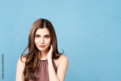 Pretty mix young Asian and Caucasian woman smiling confident in studio. Isolated blue background. Portrait long hair beautiful girl put hand on neck with happy face. Portrait for advertisement concept