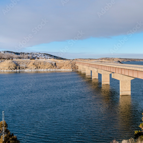 Square Bridge over lake connecting hills covered with snow on a sunny winter day