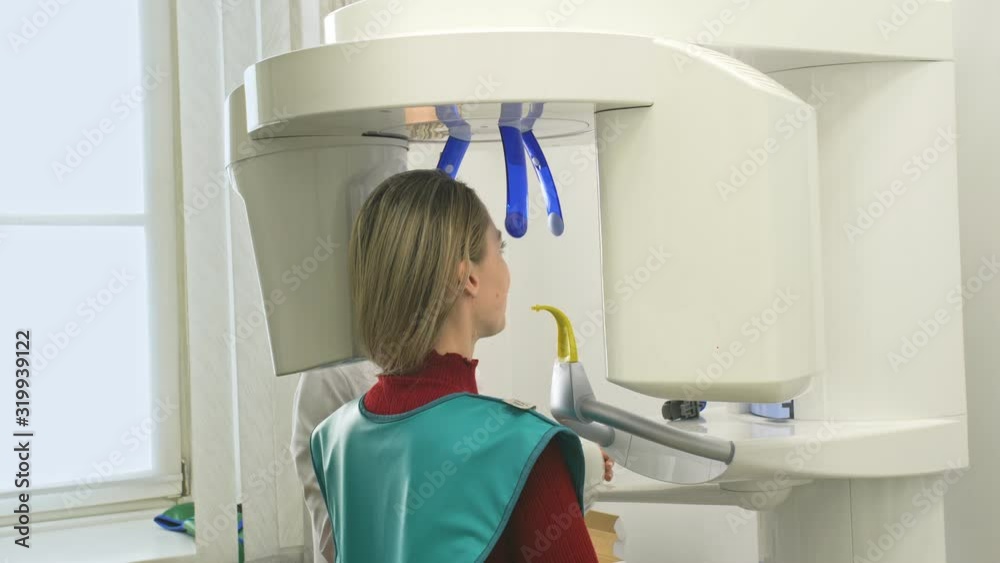 Doctor to take a image 3d scanner tomography of teeth and jaw in modern laboratory dental clinic. Female nurse shows the patient woman an x-ray machine 3d digital scanner. Computer dental diagnostics. Doctor to take a image 3d scanner tomography of teeth and jaw in modern laboratory dental clinic. Female nurse shows the patient woman an x-ray machine 3d digital scanner. Computer dental diagnostics.
