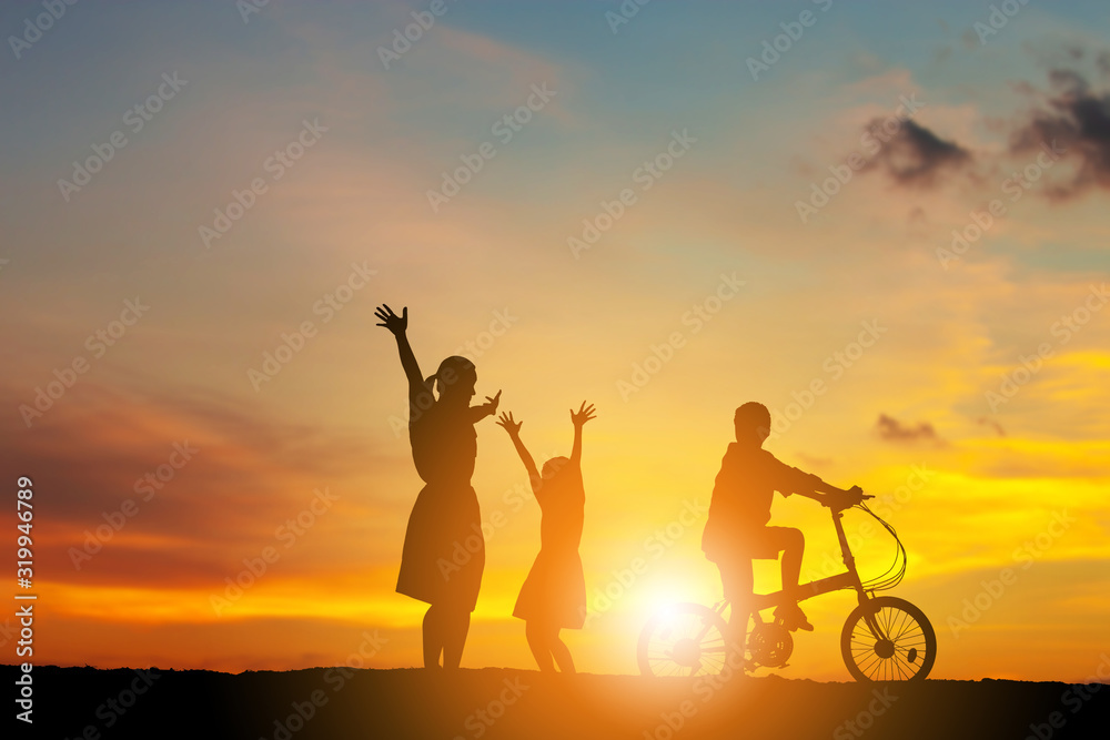 Silhouettes of mother daughter and son playing at sunset evening sky background.