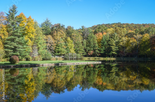 Blacksburg, Virginia, USA: Reflection of forest beside the pond under blue sky at Glen Alton Recreation Area in autumn.