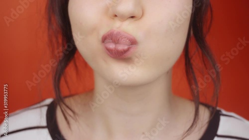 Young brunette girl with gorgeous lips on a bright red background. Happy woman sends an air kiss to the camera, lips closeup.
