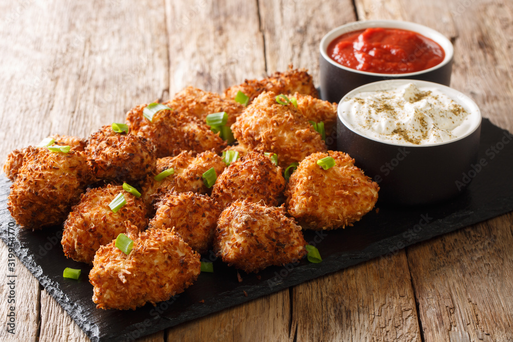 Portion Deep-fried chicken nuggets in coconut flakes served with ketchup and mayonnaise close-up on a slate board. horizontal Portion Deep-fried chicken nuggets in coconut flakes served with ketchup and mayonnaise close-up on a slate board. horizontal