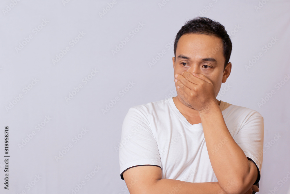 Asian youth expression wearing white T-shirt covered part of his mouth or face because he smelled something that smells or acts when he doesn't have a mask. Asian youth expression wearing white T-shirt covered part of his mouth or face because he smelled something that smells or acts when he doesn't have a mask.