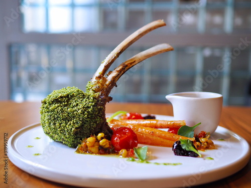 Perfectly grilled medium rare green herb crusted rack of Mottainai lamb from Australia gently prepared and served at a fine dining restaurant or cafe on white round plate on woonden table at Eureka photo