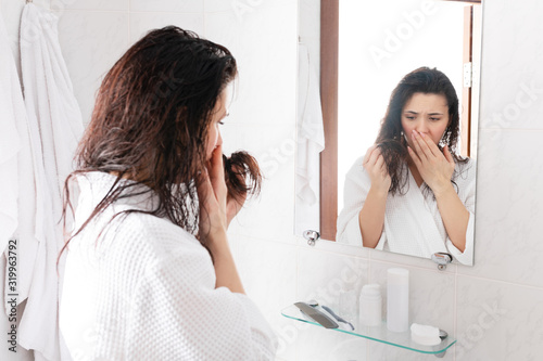 Displeased female looks at wet hair in her bathroom stay in front of mirror. Bad shampoo, hair split ends problem, hair loss trouble.