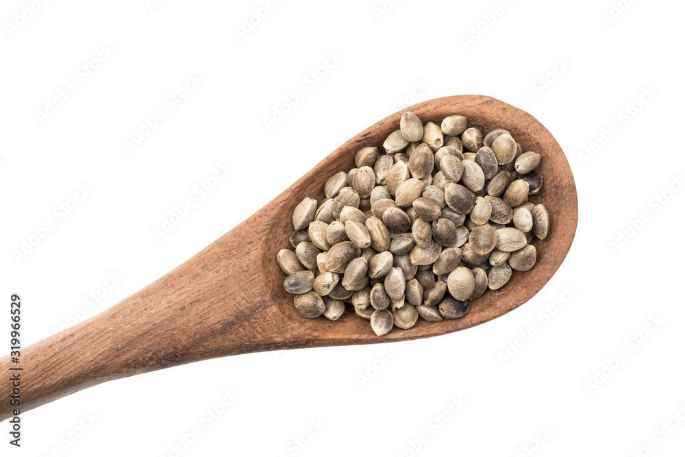 Brown wooden spoon with hemp seeds from lower left corner seen directly from above and isolated on white background
