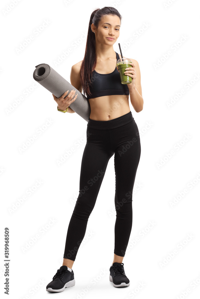 Young female in sportswear holding a healthy green shake in a cup and an exercise mat Young female in sportswear holding a healthy green shake in a cup and an exercise mat