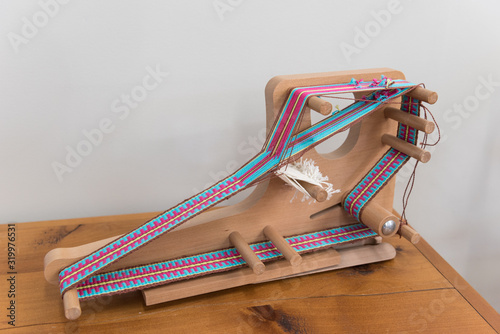 A small, tabletop, inkle loom on which a band, or strap, is in the process of being woven.