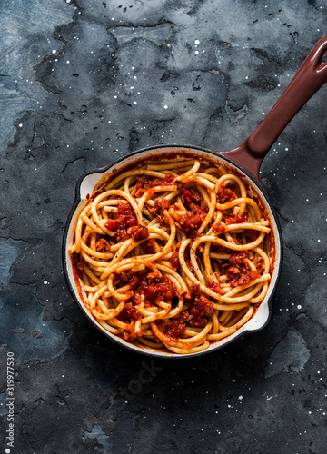 Traditional Roman pasta - bucatini amatricana in a pan on a dark background, top view photo