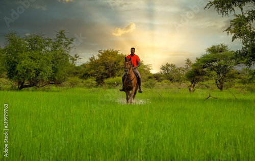 african man riding on a meadow, into the sunset