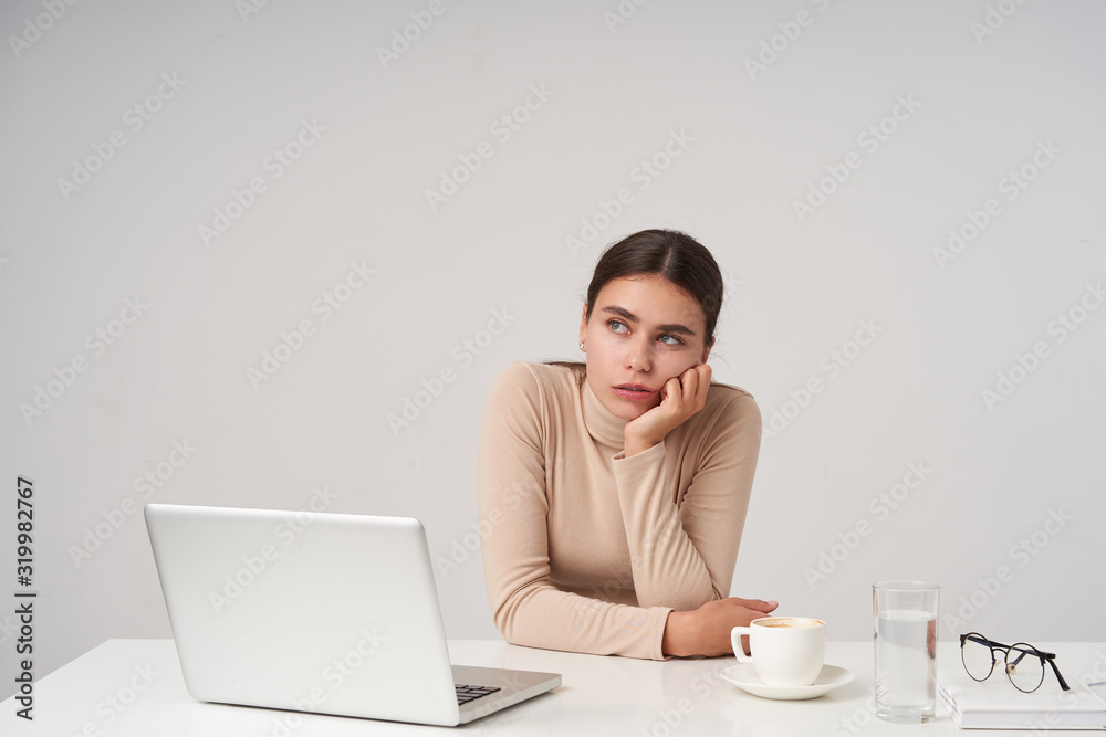 Weary young attractive dark haired lady leaning her chin on raised hand and looking dreamily aside, having long working day and counting time, isolated over white background Weary young attractive dark haired lady leaning her chin on raised hand and looking dreamily aside, having long working day and counting time, isolated over white background