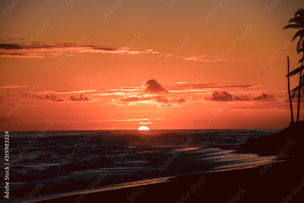 Sun is rising on the beach of a tropical island. Amazing orange orange sky and sun going up: a postcard from paradise. Scenic view, vacation concept.