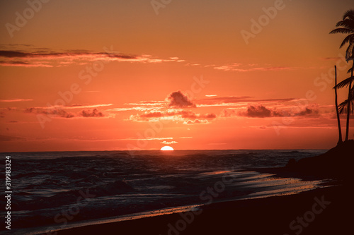 Sun is rising on the beach of a tropical island. Amazing orange orange sky and sun going up  a postcard from paradise. Scenic view  vacation concept.