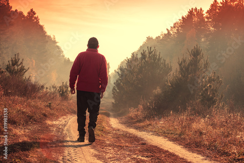 A man walks along a country road in the forest on an early foggy morning towards the sun photo